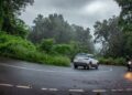 A woman driving during monsoon road trips in India, with misty green hills visible through the windshield