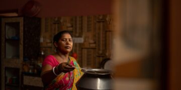 A smiling Indian woman enjoying a traditional plate of gluten-free food including dal and steamed rice at a kitchen table.