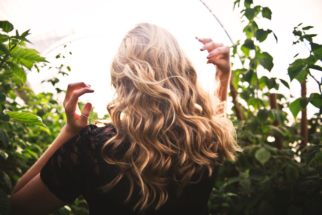 A woman applying anti-frizz serum to her damp monsoon hair in front of a bathroom mirror
