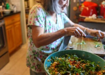 A young Indian woman sorting vegetable peels into a composting bin in her apartment kitchen