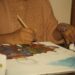 A woman carefully creating a Madhubani painting on thick white paper with a fine-tipped brush