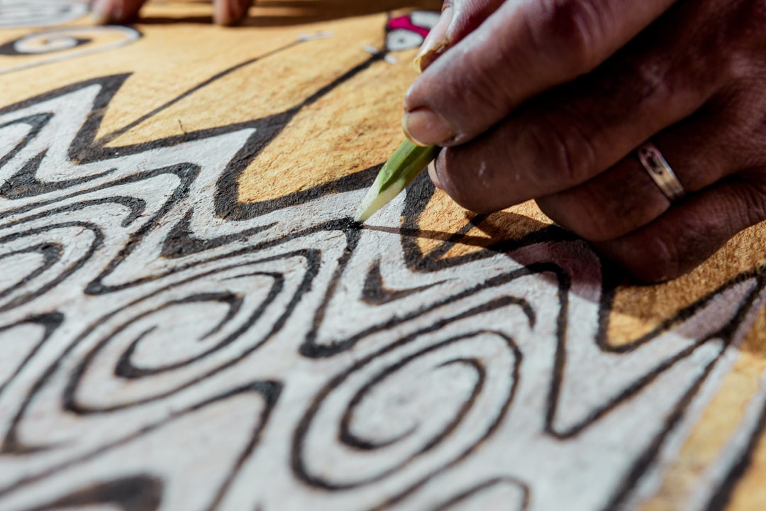 Close-up of an artist's hands practicing Warli art motifs with circles and triangles on a dark canvas