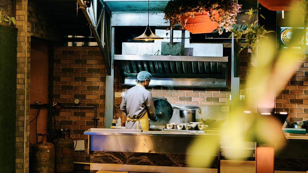 A young British Indian chef plates a regional Indian dish in a UK restaurant kitchen, representing the Indian diaspora's.