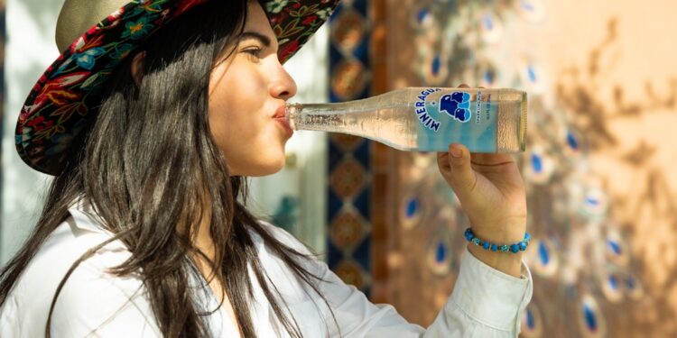 A young Indian woman drinking clean bottled water at a street market, protecting her gut health during monsoon season