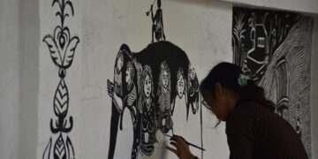 indian-woman-painting-tribal-patterns-unsplash - INDIAwebzine A woman in Maharashtra creating Warli art on brown paper using traditional white paint and a fine brush