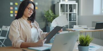 A focused Indian professional woman reviewing an annual report at her desk before making her first equity investment