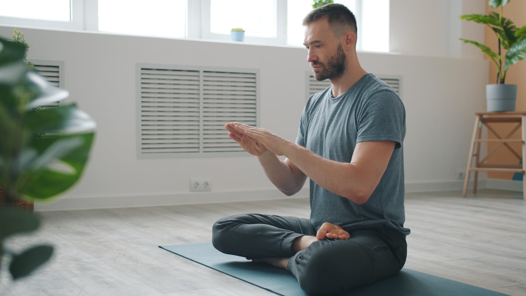 Young Indian man sitting cross-legged on floor practising pranayama breathwork with hands on knees