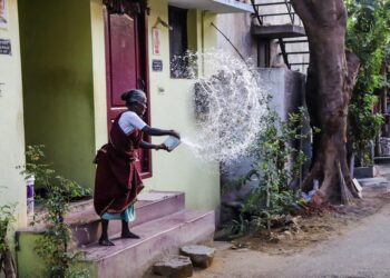 A woman using her rooftop rainwater harvesting setup during the monsoon season in an Indian home