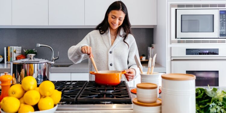 A woman stirs a pot of monsoon dal in a traditional Indian kitchen, surrounded by whole spices and steam.