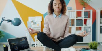 Indian woman practising pranayama breathwork at her home office desk with eyes closed