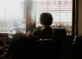 A woman sits in a cozy reading nook near a rain-streaked window, wrapped in a cotton throw, holding a book