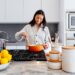 woman-terracotta-kitchen-unsplash - INDIAwebzine A smiling Indian woman arranging terracotta bowls and clay pots in a plastic-free kitchen at home