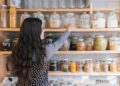 A woman carefully organising her home spice pantry with colourful Indian regional spices on a wooden shelf