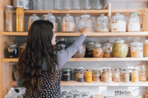 A woman carefully organising her home spice pantry with colourful Indian regional spices on a wooden shelf