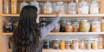 A woman carefully organising her home spice pantry with colourful Indian regional spices on a wooden shelf
