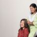 A woman performing a traditional scalp care oil massage on her long dark Indian hair at home
