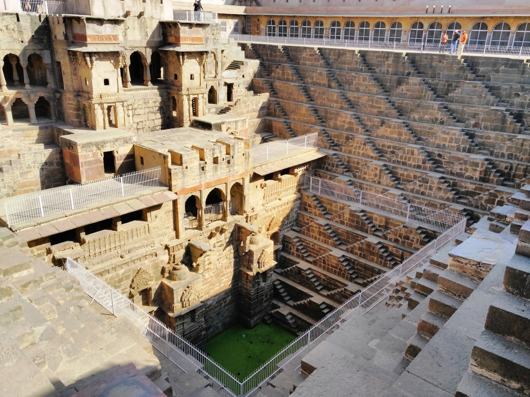 Tourists stand at the edge of a deep ancient stepwell in India, looking down at thousands of symmetrical stone steps