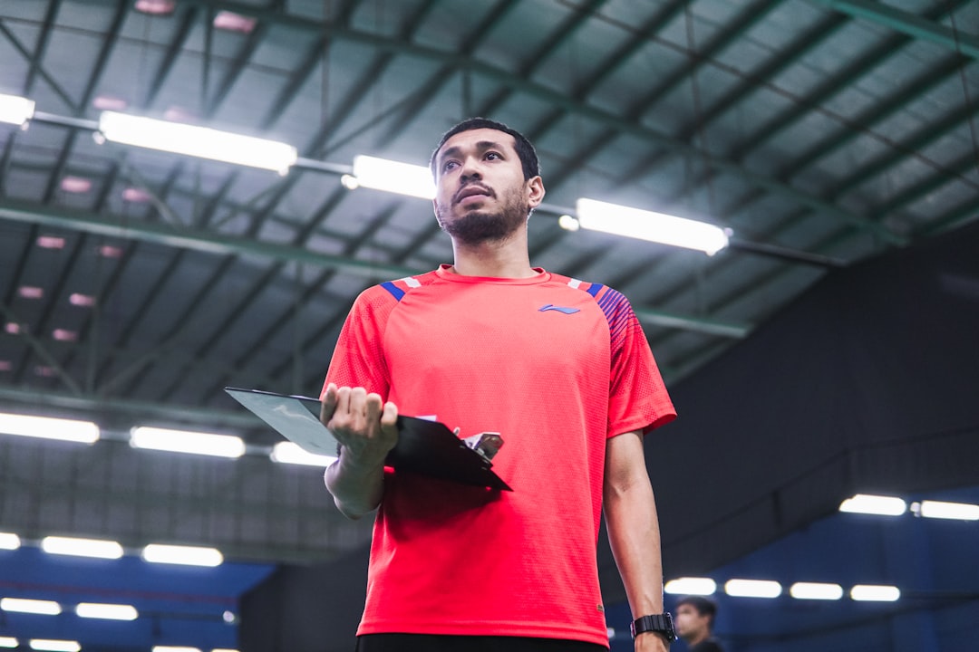 A coach observes a young Indian badminton player during an indoor academy session as part of the structured training.