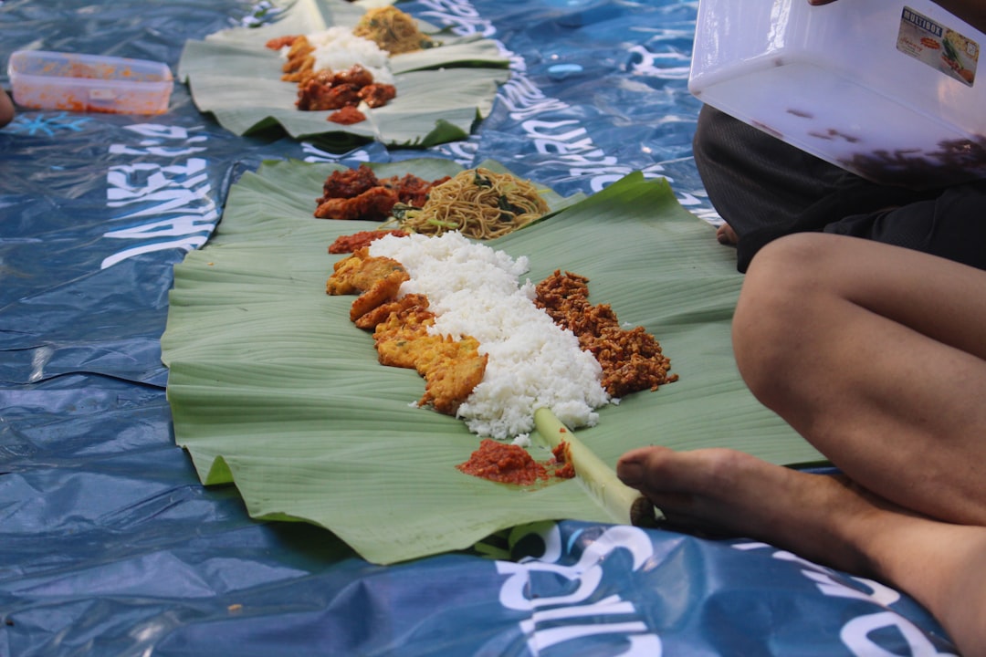A multigenerational family sits together on the floor sharing an Onam festival sadya served on banana leaves