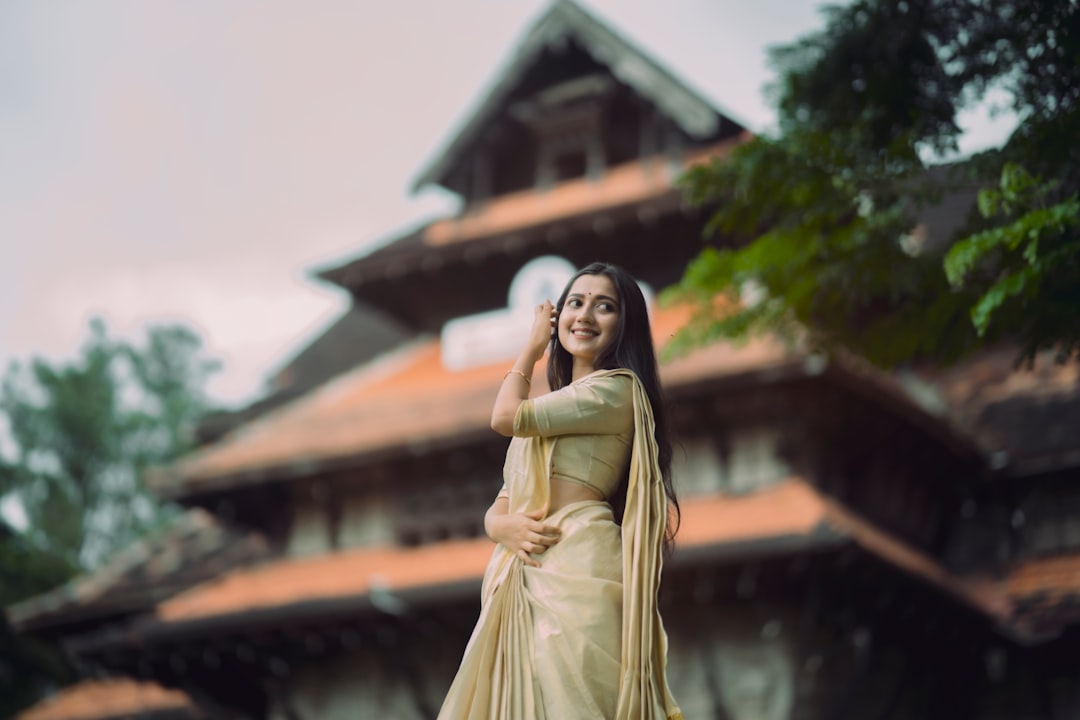 A young woman in a cream and gold kasavu saree smiles warmly during an Onam festival cultural gathering