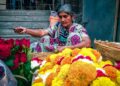A woman carefully places flowers to create a pookalam design during the Onam festival celebration at her home entrance