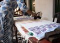 A woman carefully pressing an Indian carved wooden stamp onto cotton fabric during a block printing session at home