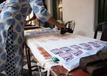 A woman carefully pressing an Indian carved wooden stamp onto cotton fabric during a block printing session at home