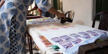 A woman carefully pressing an Indian carved wooden stamp onto cotton fabric during a block printing session at home