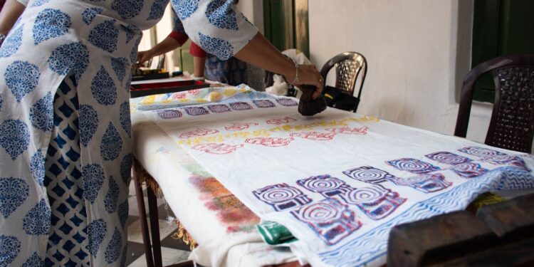 woman-pressing-wooden-stamp-fabric-unsplash - INDIAwebzine A woman carefully pressing an Indian carved wooden stamp onto cotton fabric during a block printing session at home