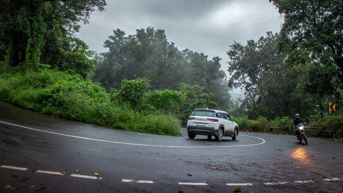 Una mujer conduciendo durante los viajes por carretera del monzón en India, con colinas verdes brumosas visibles a través del parabrisas