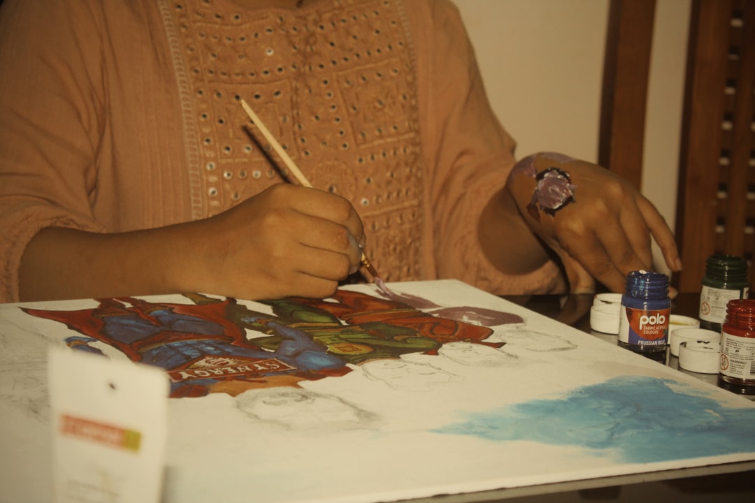 Una mujer creando cuidadosamente una pintura Madhubani sobre papel blanco grueso con un pincel de punta fina