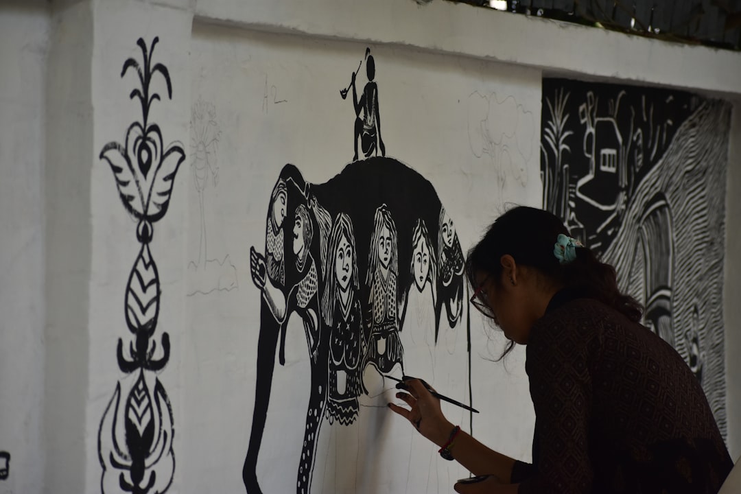Una mujer en Maharashtra creando arte Warli en papel marrón usando pintura blanca tradicional y un pincel fino