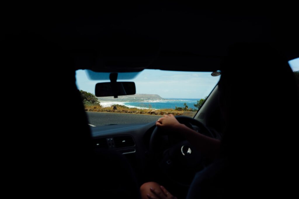 Un viajero en la carretera disfrutando de los viajes costeros en India con colinas verdes y el Mar Arábigo visibles a través del parabrisas